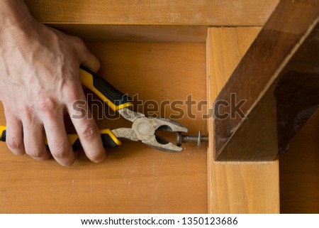 The hands of a carpenter repairing old furniture with pliers tool,