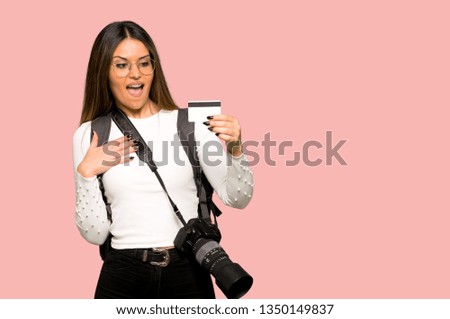 Young photographer woman holding a credit card on isolated pink background