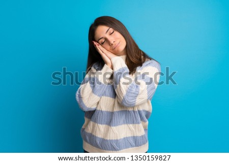 Young woman over blue wall making sleep gesture in dorable expression