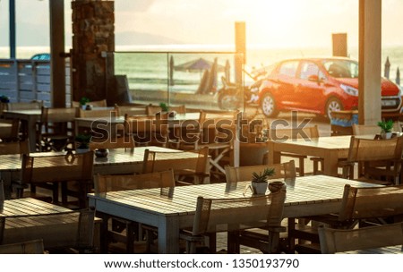 Beach cafe by sea at sunset on waterfront with parked cars beach. Depth of field, focus blur, beige toning, Crete, Greece