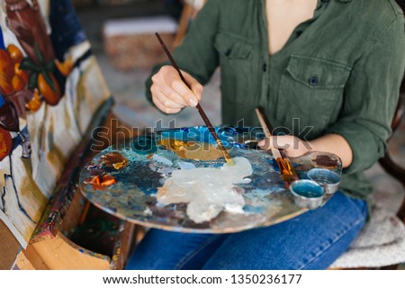 Close up beautiful woman hands holding paint brush drawing amazing picture on canvas in modern cozy art workshop