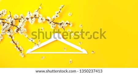 White wooden hanger hanging on the spring flowering branch on yellow background. Spring sale concept discount store shopping empty hanger. Creative fashion beauty banner. Flat lay top view copy space.