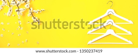 White wooden hangers and spring flowering branch on yellow background. Spring sale concept discount store shopping empty hanger promo design Creative fashion beauty banner Flat lay top view copy space