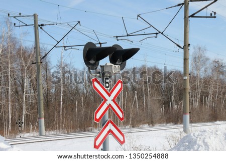 sign railway crossing with signal lights in winter, against the forest, blue Sunny sky. Supports of contact network.