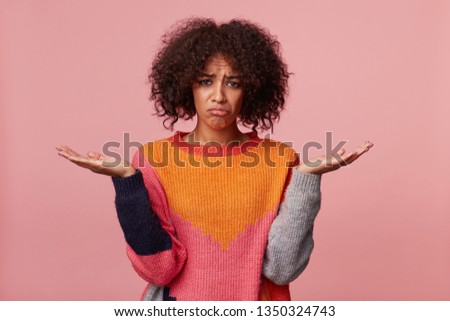 Girl with afro hairstyle looking helpless offended sad upset, in bad mood, stand with palms raised up holding a copy space, pouted her lips, feels injustice hopelessness, isolated on pink Royalty-Free Stock Photo #1350324743