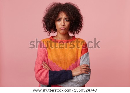 Brunette girl with afro hairstyle offended sad upset, pouted her lips, is overwhelmed with negative emotions, in bad mood, stand with arms crossed, wearing colorful sweater, isolated on pink Royalty-Free Stock Photo #1350324749