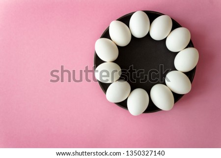 white eggs lie on a dark plate in a circle around the shape of a flower, on a pink pastel background. Happy Easter.