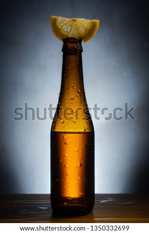 Glass bottle of cool beer with a slice of lemon on a gray background. Minimalistic style of brutal male still life.