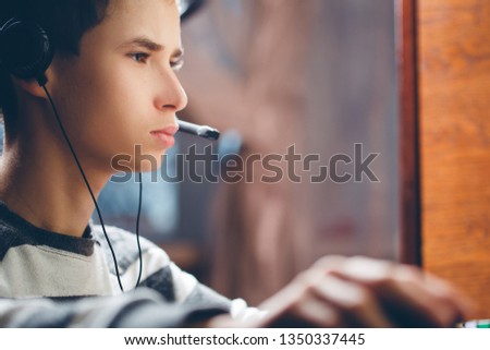 boy in headphones with microphone plays laptop at the game, child communicates on the Internet via web camera, there is lot of noise in the photo that adds atmosphere