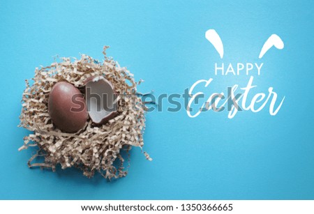 It is a picture of a blue background with a happy Easter text with elements of the holiday eggs of chocolate in a nest and ears of a rabbit