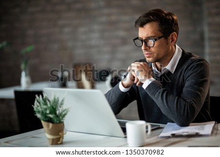 Dedicated entrepreneur sitting at office desk and reading an e-mail while working on a computer.  Royalty-Free Stock Photo #1350370982