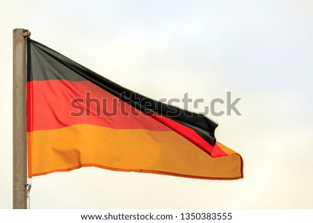Flag of Germany - national symbol in wind. German flag in front of dark clouds with blurred wind effect. Flag of Germany waving in wind against white cloudy blue sky. German flag on flagpole.