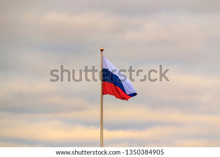 Flag of Russia - national symbol in wind.  russian flag in front of dark clouds with blurred wind effect. Flag of Russia waving in the wind against white cloudy blue sky. russian flag on flagpole.