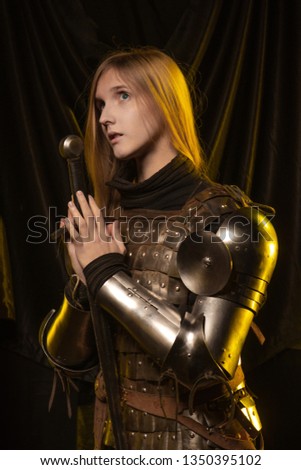 Blonde girl in medieval knight's armor 15th century in yellow light against a dark background