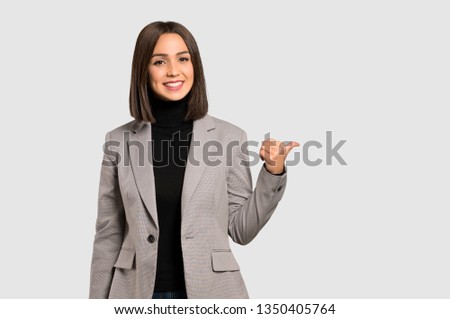 Young business woman pointing to the side to present a product on isolated grey background