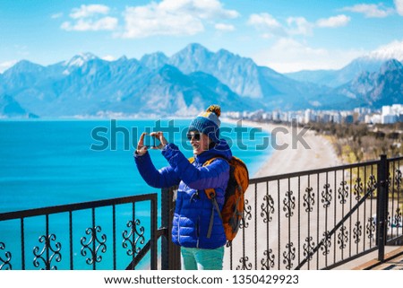 A girl takes a selfie on the waterfront. A woman walks through the resort town and takes pictures. Brunette travels around the Turkish city in winter. Photo on the background of the sea and mountains.