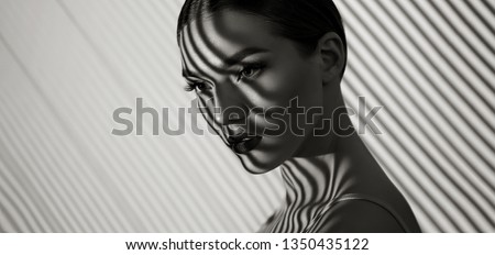 Black and white portrait of a beautiful young girl with a shadow pattern on the face and body in the form of stripes.fashion, beauty, makeup, cosmetics, beauty salon, style, personal care, posture. Royalty-Free Stock Photo #1350435122