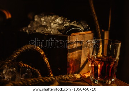 Horizontal photo of a glass of rum on an old chest of drawers in an old chest of ice and rope-pirate mood