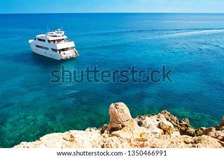Image of one big white yacht in the water near Cape Greco, Cyprus. Rock coastline near deep green transparent azure water. Warm day in fall