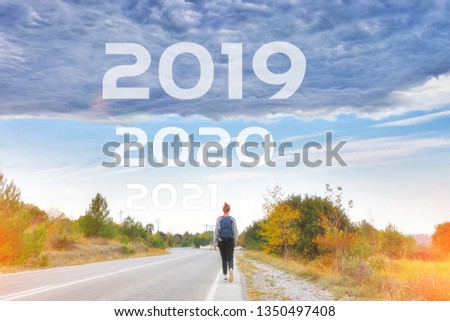 Woman traveler walking alone along road to goals 2020 2021 new year. Danger to 2019 year concept with rainstorm clouds. Success passing time, future concept Empty asphalt road Leaving behind old years Royalty-Free Stock Photo #1350497408