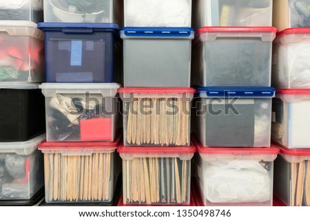 Stacked plastic file storage boxes with folders, binders and miscellaneous items.   Royalty-Free Stock Photo #1350498746