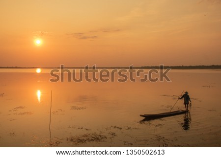 Beautiful sunset , nice and warm sky, there are two silhouette fishermen on boat in the small reservoir with a nice bank background.
