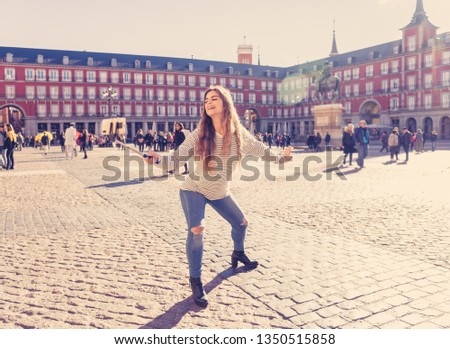 Beautiful young caucasian woman happy and excited in Plaza Mayor Madrid taking a selfie or video on mobile smart phone and stick having fun. In travel and surf the world , tourism, student lifestyle.