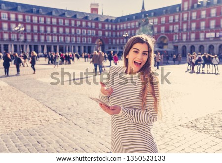 Beautiful young student tourist woman happy and excited in Plaza Mayor Madrid Looking at travel mobile app or checking smart phone to find directions. In tourism and technology, travel around Europe.
