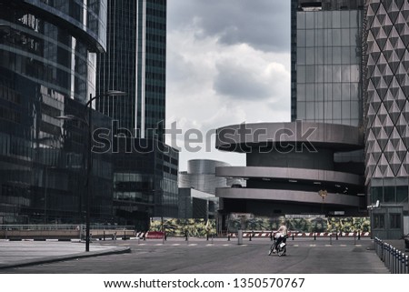 Moscow City skyscrapers in summer in cloudy weather after the rain and a girl on a bike looking on these huge buildings