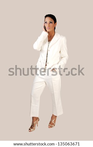 A young pretty business woman in a white suit standing for light gray background, talking on her cell phone.