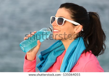 Fitness woman drinking and resting after training outdoors. Beautiful caucasian girl sitting and relaxing after exercising. Copy space.
