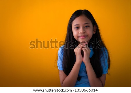 Portrait of lovely happy girl isolated orange background, Asian long hair young girl holding hers hands together under hers face.
