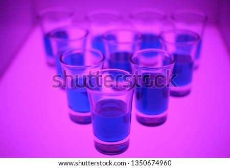 A blue drink in a shot glasses is bowling line up in a light box.