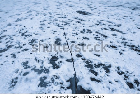 Frozen water surface. Ice on a mountain lake. Cracked on ice. Cracked on the surface of a frozen lake. Snow on ice. Air bubbles in the ice. The texture of the frozen surface of the water.