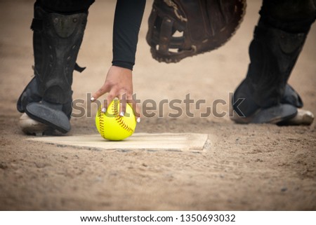 Catcher with painted finger nails grabbing a neon softball off home plate, in a sports background with space for text on bottom