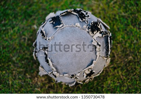 Torn football on the grass lawn. Soccer ball skin torn on the field, but still in use for play.