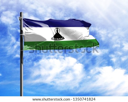 National flag of Lesotho on a flagpole in front of blue sky.