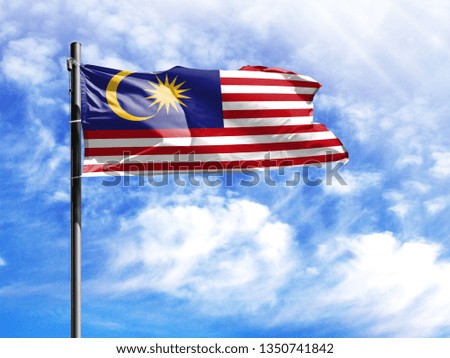 National flag of Malasia on a flagpole in front of blue sky.
