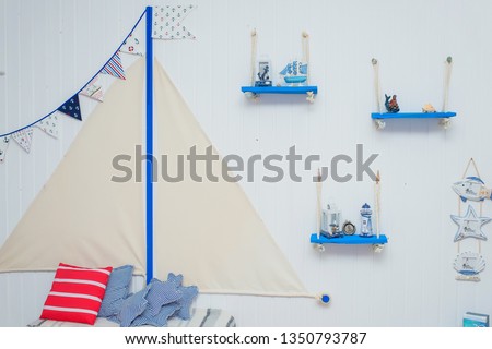 Interior decor in the marine style. Paper garland on the background of bright walls. Blue wooden shelves on ropes.