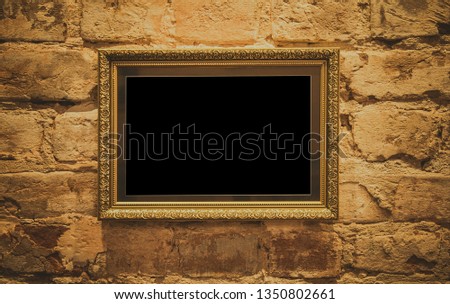 A golden frame with a beautiful decorative baguette hangs on a golden antique wall in vintage style.