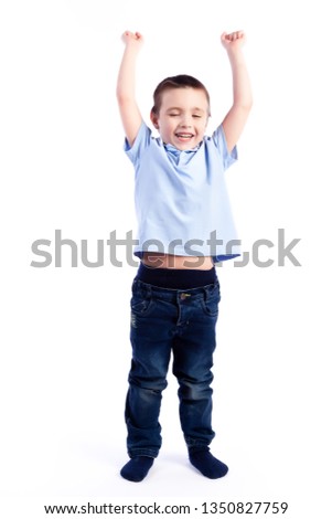 Little smiling boy with dark hair in blue jeans, blue polo t-shirt is jumping and having fun on an isolated white background in a photo studio