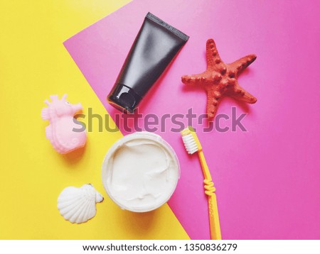 Toothpaste with activated carbon in a black tube, a yellow toothbrush and a can of white clay for skin care on a pink background. Flat lay beauty photo