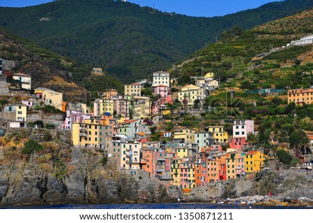 Colourful houses nestle in a V-shaped valley below steep mountain terraces. View from the sea to Riomaggiore village in the Cinque Terre, Italy. 