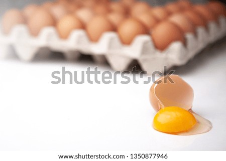 
A tray of whole chicken eggs and one broken on a white background.