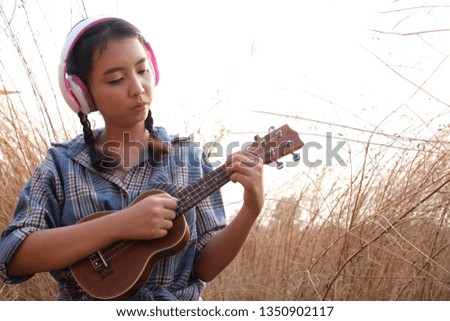 Asia young girl in headphones listening music and play Ukulele at field grass