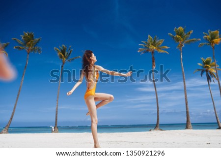 A woman in a swimsuit bounces up in the sand among palm trees                