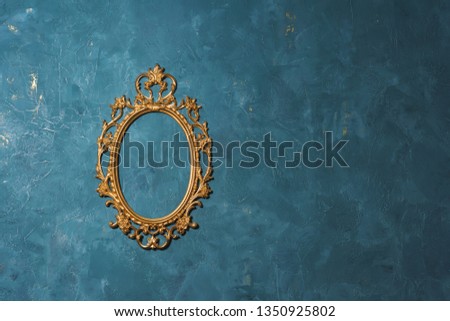 Gold frame on blue wall background. Decorative element. Vintage gilded frame for the mirror. Vintage photo zone. Forged metal product.