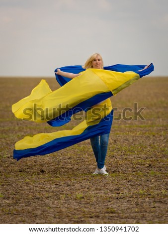 Young amazing beautiful girl with a huge Ukrainian flag on the field. Ukraine's Independence Day.