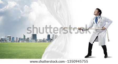 Conceptual image of successful doctor on white medical suit pulling white curtain while standing on white background with urban city view behind white fabric