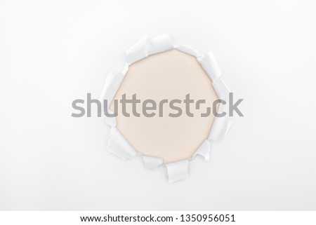 ripped hole in white textured paper on ivory background 